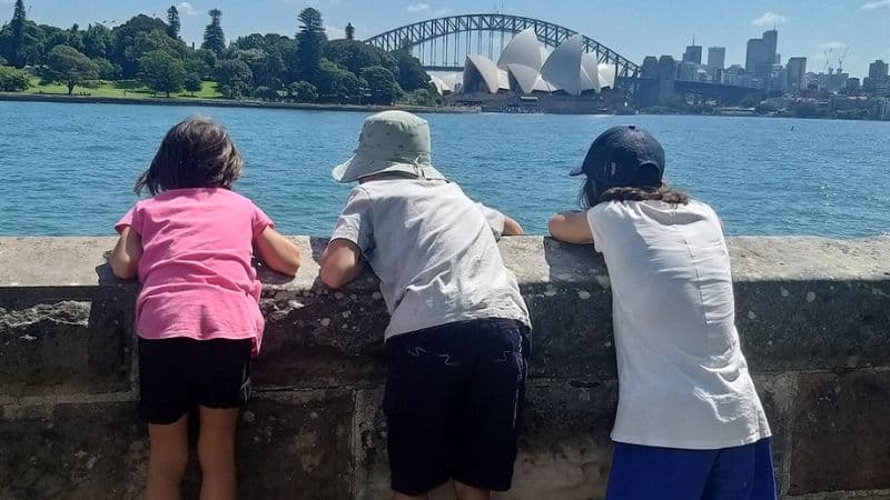 シドニーオペラハウスとハーバードブリッジを遠くから眺めている3人の子どもの後ろ姿の写真